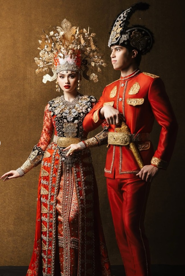 Kedua calon pengantin tampil kompak dalam balutan busana bernuansa merah. Busana adat tersebut semakin terlihat mewah dengan detail bordir dan ornamen emas. Foto: Instagram/@thebridestory