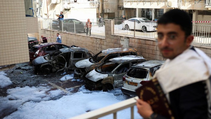 Emergency personnel work next to burnt-out vehicles at an impact site, following a barrage of missiles launched from Iran, amid the U.S.-Israeli conflict with Iran, in Petach Tikva, Israel, April 6, 2026. REUTERS/Florion Goga