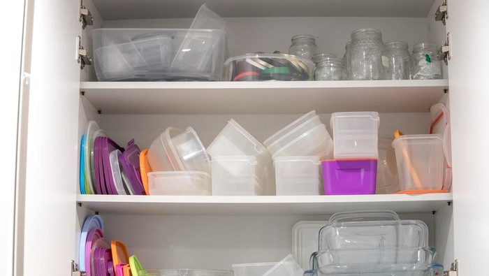 Open kitchen cupboard full of plastic and glass containers inside.