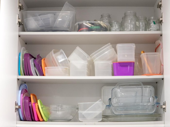 Open kitchen cupboard full of plastic and glass containers inside.