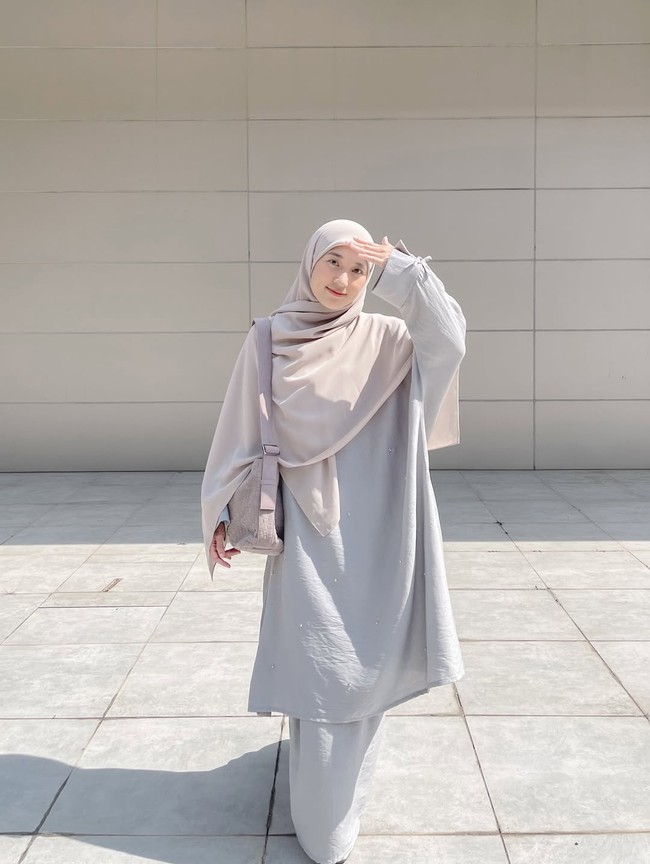 Setelan tunik dan rok berwarna abu-abu muda ini memberikan siluet yang ramping namun tetap sesuai kaidah syari. Penggunaan khimar dengan material jatuh membuat tampilan ini terlihat sangat nyaman untuk aktivitas sehari-hari di cuaca panas. Foto: Dok. Instagram @denisarani.