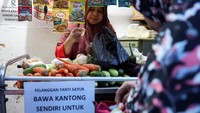 Seorang pedagang sayur bernama Yamiati, 61, tetap melayani pembeli di tokonya. Ia memasang imbauan agar pelanggan membawa tas belanja sendiri. REUTERS/Ajeng Dinar Ulfiana