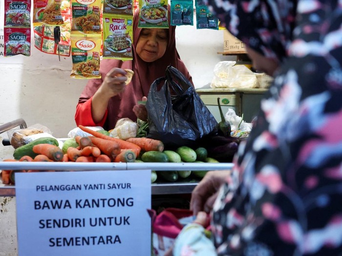 Yamiati, 61, serves a customer at her vegetable shop near a sign urging customers to bring their own shopping bags, amid rising plastic prices in Depok, on the outskirts of Jakarta, Indonesia, April 9, 2026. REUTERS/Ajeng Dinar Ulfiana