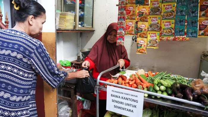 Yamiati, 61, serves a customer at her vegetable shop near a sign urging customers to bring their own shopping bags, amid rising plastic prices in Depok, on the outskirts of Jakarta, Indonesia, April 9, 2026. REUTERS/Ajeng Dinar Ulfiana