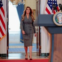 Saat berbicara di podium konferensi pers di Gedung Putih Kamis (9/4/2026), Melania Trump tampil mengenakan setelan blazer dan rok pensil berwarna abu-abu. Foto: REUTERS/Evan Vucci