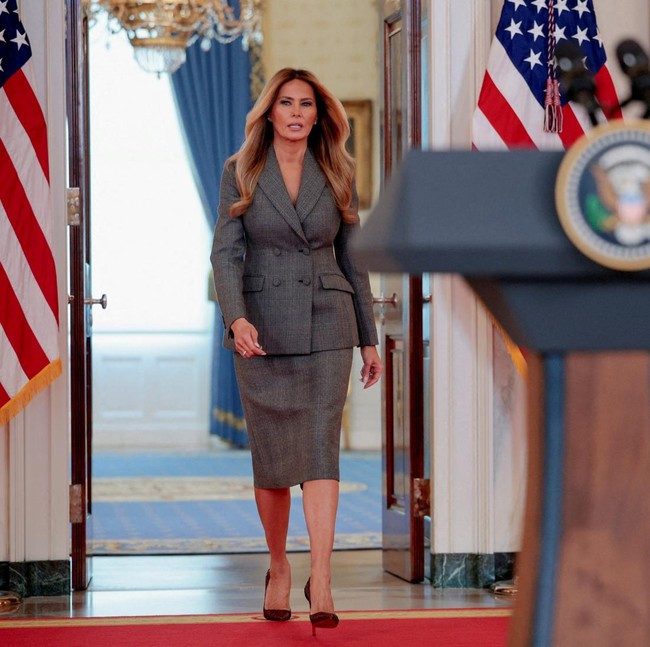 Saat berbicara di podium konferensi pers di Gedung Putih Kamis (9/4/2026), Melania Trump tampil mengenakan setelan blazer dan rok pensil berwarna abu-abu. Foto: REUTERS/Evan Vucci