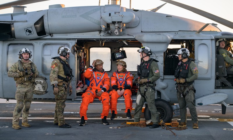 NASA astronaut Victor Glover, Artemis II pilot, left, and NASA astronaut Christina Koch, Artemis II mission specialist are seen sitting on a Navy MH-60 Seahawk from Helicopter Sea Combat Squadron (HSC) 23 on the flight deck of USS John P. Murtha after they and fellow crewmates CSA (Canadian Space Agency) astronaut Jeremy Hansen, Artemis II mission specialist, and NASA astronaut Reid Wiseman, Artemis II commander, were extracted from their Orion spacecraft after splashdown, Friday, April 10, 2026, in the Pacific Ocean off the coast of California. NASA’s Artemis II mission took the quartet on a nearly 10-day journey around the Moon and back to Earth. Following a splashdown at 5:07 p.m. PDT (8:07 p.m. EDT), NASA, U.S. Navy, and U.S. Air Force teams are working to bring the Orion spacecraft aboard the recovery ship.