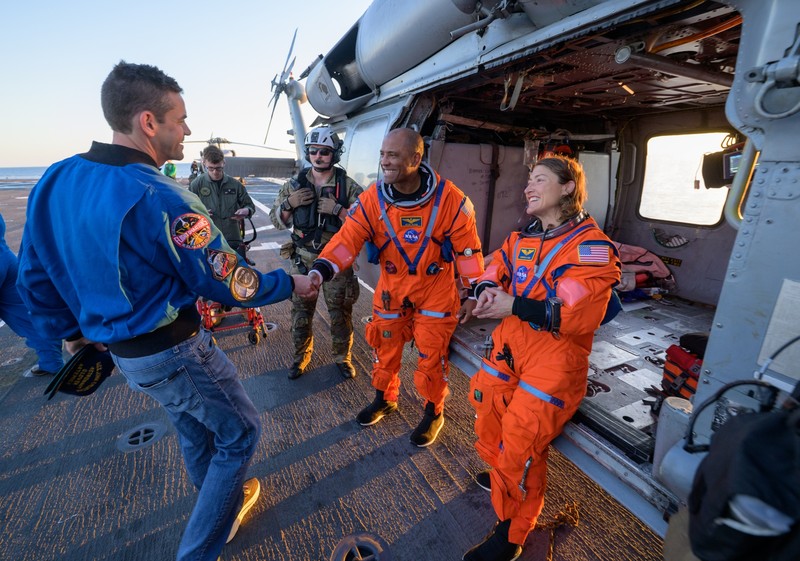 NASA astronaut Victor Glover, Artemis II pilot, left, and NASA astronaut Christina Koch, Artemis II mission specialist are seen sitting on a Navy MH-60 Seahawk from Helicopter Sea Combat Squadron (HSC) 23 on the flight deck of USS John P. Murtha after they and fellow crewmates CSA (Canadian Space Agency) astronaut Jeremy Hansen, Artemis II mission specialist, and NASA astronaut Reid Wiseman, Artemis II commander, were extracted from their Orion spacecraft after splashdown, Friday, April 10, 2026, in the Pacific Ocean off the coast of California. NASA’s Artemis II mission took the quartet on a nearly 10-day journey around the Moon and back to Earth. Following a splashdown at 5:07 p.m. PDT (8:07 p.m. EDT), NASA, U.S. Navy, and U.S. Air Force teams are working to bring the Orion spacecraft aboard the recovery ship.