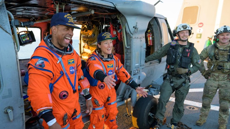NASA astronaut Victor Glover, Artemis II pilot, left, and NASA astronaut Christina Koch, Artemis II mission specialist are seen sitting on a Navy MH-60 Seahawk from Helicopter Sea Combat Squadron (HSC) 23 on the flight deck of USS John P. Murtha after they and fellow crewmates CSA (Canadian Space Agency) astronaut Jeremy Hansen, Artemis II mission specialist, and NASA astronaut Reid Wiseman, Artemis II commander, were extracted from their Orion spacecraft after splashdown, Friday, April 10, 2026, in the Pacific Ocean off the coast of California. NASA’s Artemis II mission took the quartet on a nearly 10-day journey around the Moon and back to Earth. Following a splashdown at 5:07 p.m. PDT (8:07 p.m. EDT), NASA, U.S. Navy, and U.S. Air Force teams are working to bring the Orion spacecraft aboard the recovery ship.