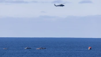 Sebuah helikopter MH-60 Seahawk dari HSC-23 terbang di atas saat perahu kecil tim recovery NASA dan US Navy mendekati Orion spacecraft Artemis II setelah splashdown di Samudra Pasifik lepas pantai California, Foto: NASA