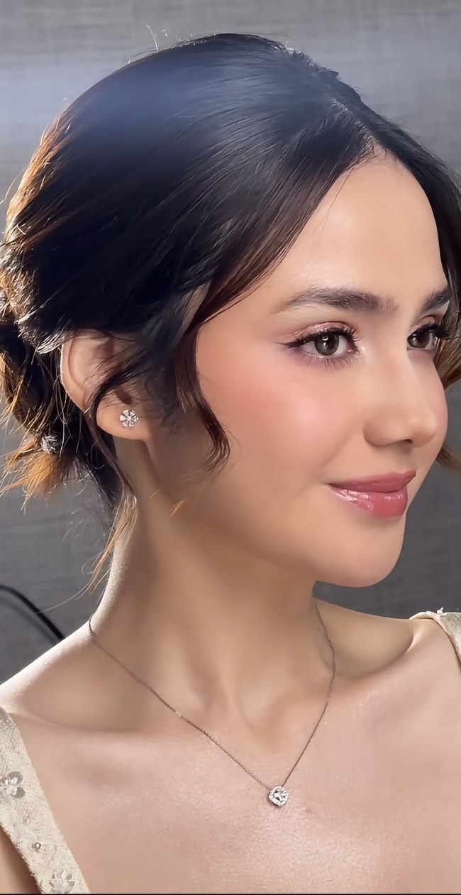 Riasan wajahnya terlihat flawless dengan soft glam look yang natural. Kulit tampak glowing dengan foundation ringan. Riasan mata tidak berlebihan, fokus pada bulu mata lentik dan eyeliner tipis. Blush on pink menambah efek segar, serta lipstik berwarna nude pink menambah kesan manis. Foto: Instagram/@syifahadju