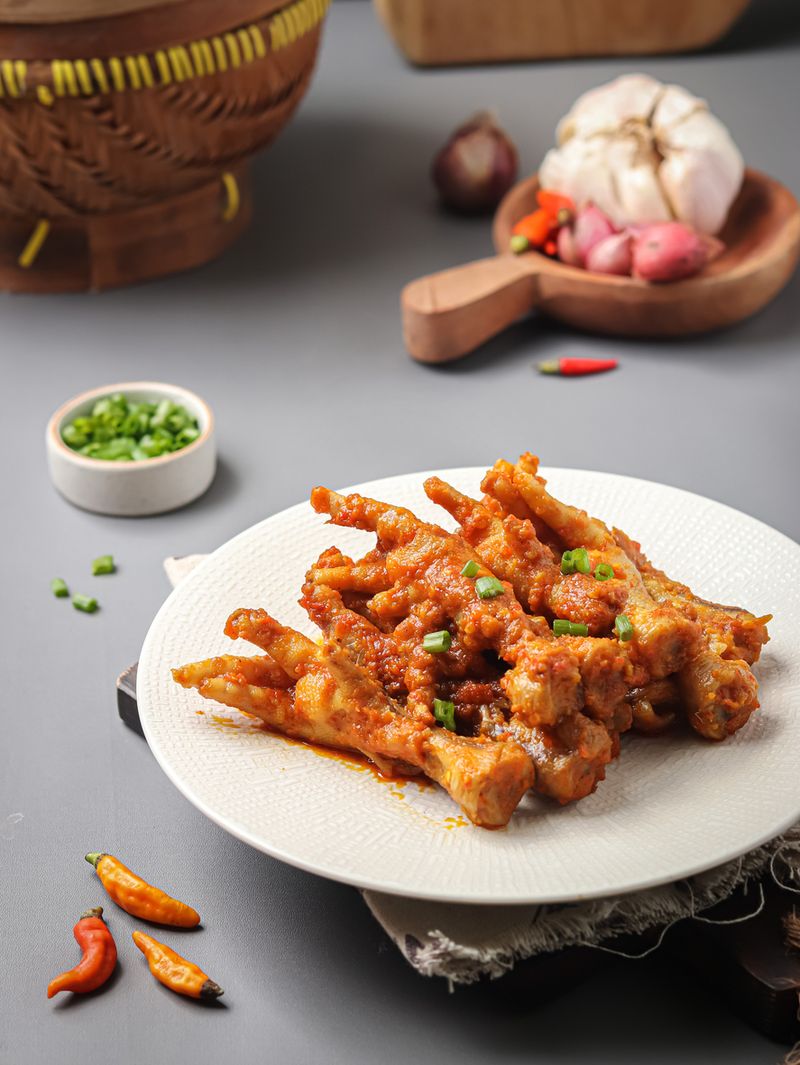 Ceker Mercon Spicy chicken claw (ceker ayam pedas) with spices, red chili, garlic, candlenut. served on a serving plate on a gray background and a sprinkling of scallions