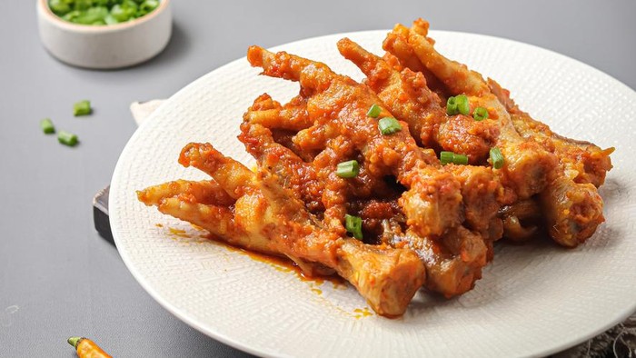 Spicy chicken claw (ceker ayam pedas) with spices, red chili, garlic, candlenut. served on a serving plate on a gray background and a sprinkling of scallions
