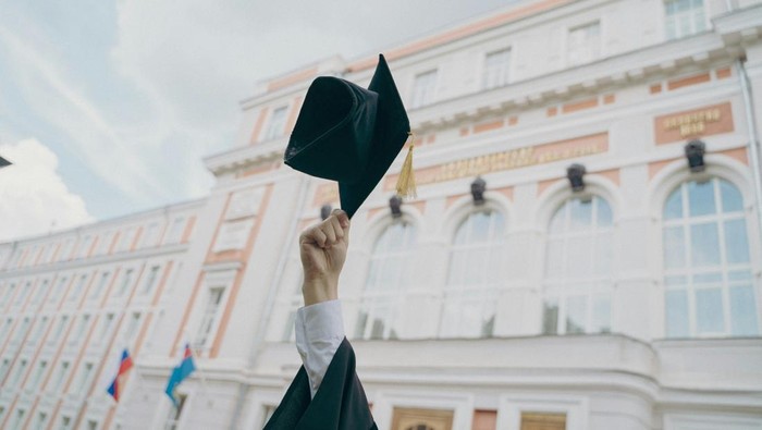 Tangan mengangkat topi wisuda. Daftar PTS terbaik Jogja 2026 versi EduRank. 