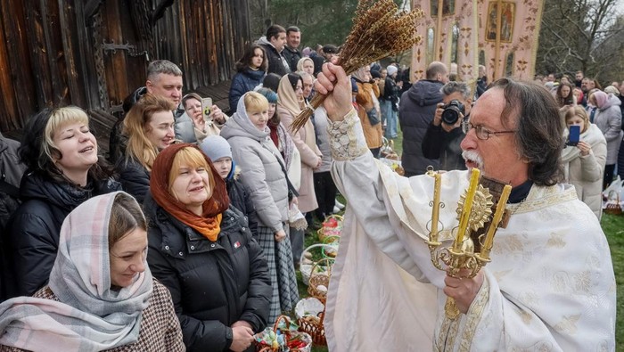 Believers react as a priest blesses by sprinkling holy water during an Orthodox Easter service, following a 32‑hour ceasefire declared by Russia, amid Russias attack on Ukraine, near the church at the National Museum of Folk Architecture in Kyiv, 