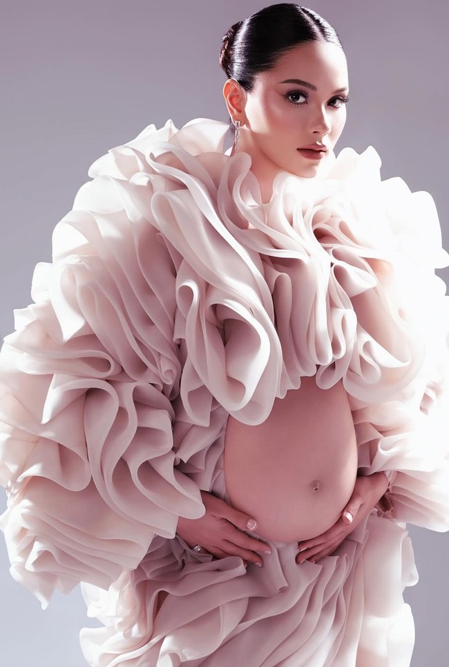 Gaun berwarna nude pink itu memiliki potongan tak biasa. Bagian perut dibuuat terbuka (cut-out) untuk menonjolkan bare baby bump. Foto: Instagram/@alyssadaguise