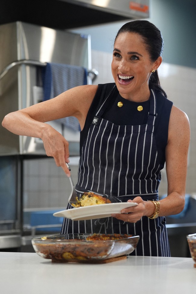 Lawatan kemudian berlanjut ke rumah penampungan tunawisma di mana Meghan menyiapkan makanan langsung di dapur. Busana yang sama masih dipakai, tapi kali ini dilapisi celemek. (Foto: Jonathan Brady/Pool via REUTERS)