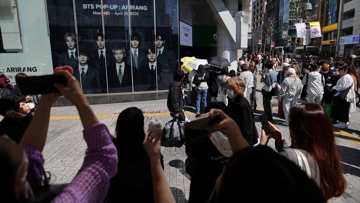 A fan of Kpop boy band BTS poses before the poster depicting the members at a pop-up store, ahead of the band's upcoming BTS World Tour 'Arirang' concert, at Shibuya shopping and amusement district in Tokyo, Japan, April 16, 2026. REUTERS/Issei Kato