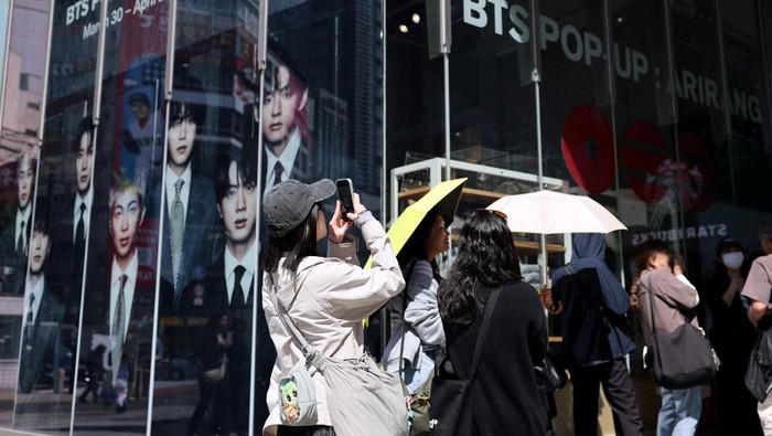 A fan of Kpop boy band BTS poses before the poster depicting the members at a pop-up store, ahead of the band's upcoming BTS World Tour 'Arirang' concert, at Shibuya shopping and amusement district in Tokyo, Japan, April 16, 2026. REUTERS/Issei Kato