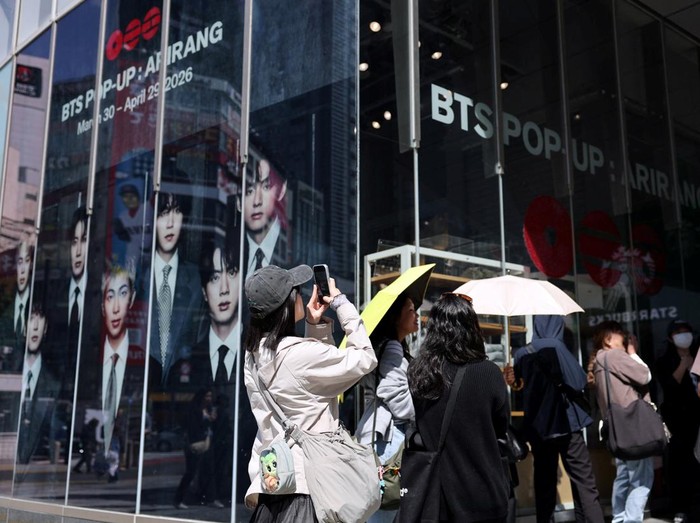 A fan of Kpop boy band BTS poses before the poster depicting the members at a pop-up store, ahead of the bands upcoming BTS World Tour Arirang concert, at Shibuya shopping and amusement district in Tokyo, Japan, April 16, 2026. REUTERS/Issei Kato