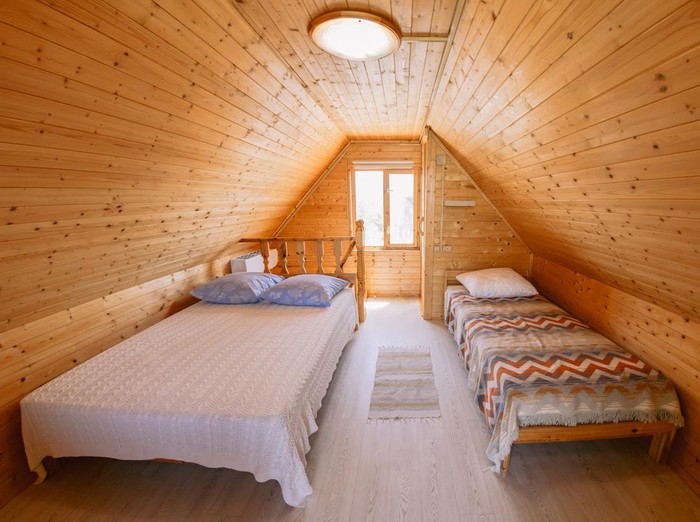 Cozy attic bedroom with wooden walls, two beds, soft light, and warm rustic interior