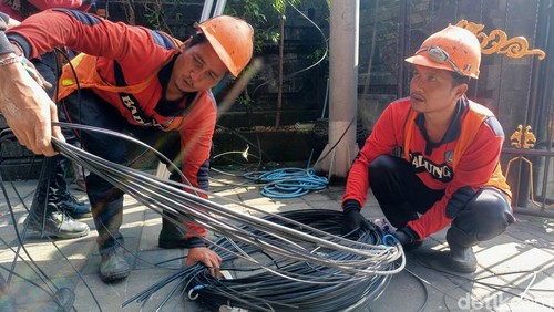 Petugas Dinas PUPR Badung merapikan kabel optik yang sudah diturunkan di Jalan Raya Basangkasa, Badung, Jumat (24/4/2026).
