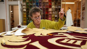 Pengerjaan berlangsung di Royal School of Needlework di London. Ini merupakan kolaborasi antara Royal School of Needlework, yang timnya menjahit dekorasi sudut yang menggambarkan sandi - inisial C dan R, nomor pemerintahan Charles dalam angka Romawi ditambah mahkota Tudor - dan spesialis peralatan panggung Jerman, Gerriets, yang membuat tirai merah tua. Foto: REUTERS/Isabel Infantes