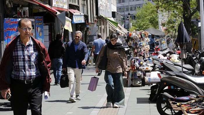 Orang-orang berjalan di sudut keramaian di Teheran, dan seorang perempuan muda membawa tas belanja. (Getty Images)