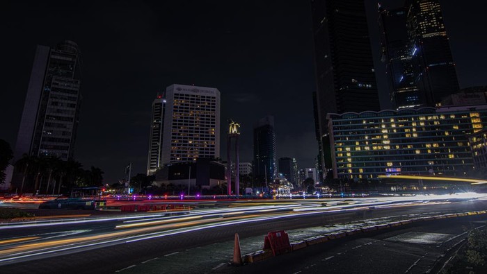 Sejumlah kendaraan melintasi kawasan Bundaran HI saat pemadaman lampu di Jakarta, Sabtu (25/4/2026). Pemerintah Provinsi DKI Jakarta melakukan pemadaman lampu selama satu jam di sejumlah jalan protokol pada pukul 20.30 hingga 21.30 WIB dalam rangka m
