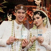 Syifa mengenakan kebaya pengantin berwarna putih dengan detail bordir dan payet yang halus. Siluetnya fitted mengikuti tubuh, dengan lengan panjang transparan yang dihiasi sulaman elegan. Bagian bawahnya memanjang membentuk train yang dramatis namun tetap lembut, menambah kesan mewah tanpa berlebihan. Foto: Instagram/@syifahadju