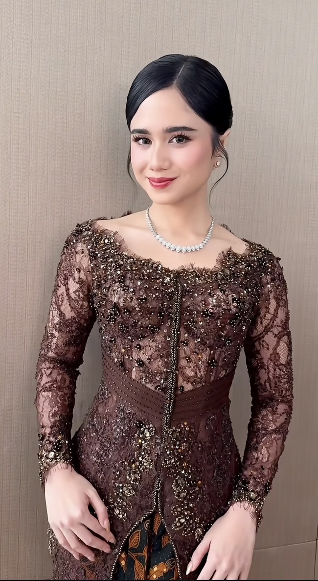 Riasan wajahnya yang flawless dan natural merupakan hasil tangan dari MUA Nooi Beauty. Complexion terlihat halus dengan hasil akhir glowing, dipadukan dengan blush on lembut yang memberi kesan segar. Riasan mata dibuat tegas namun tetap soft dengan bulu mata lentik dan eyeshadow bernuansa cokelat. Sementara itu, lipstik warna merah muda memberikan sentuhan manis yang menyempurnakan keseluruhan tampilan. Foto: Instagram/@nooibeauty
