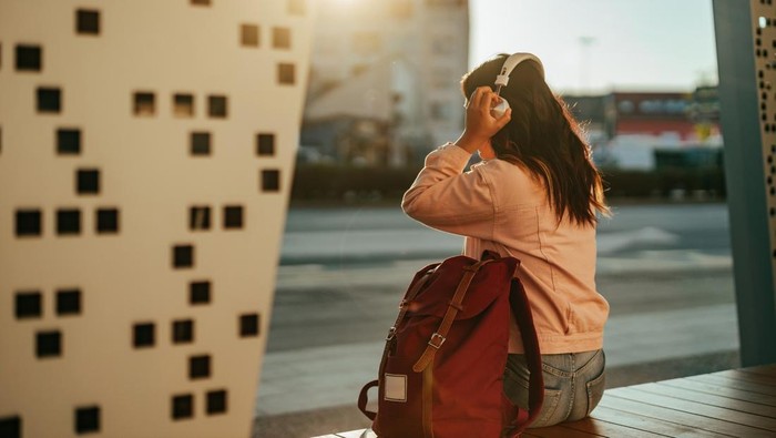 Female sitting outside and listening her favorite music while waiting for the train