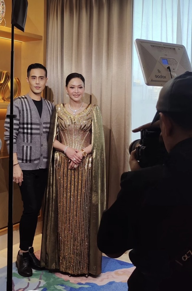 Di acara resepsi orangtua El dan Syifa kompak kenakan busana berwarna keemasan rancangan desainer Wiki Wu. Maia tampil glamor dengan gaun berwarna emas berpotongan leher v neck. Gaun tersebut dihiasi pola garis-garis vertikal dan lengkungan emas. Bagian lengannya memiliki potongan seperti jubah yang membuat penampilannya makin classy. Foto: Instagram/@wikiwu5