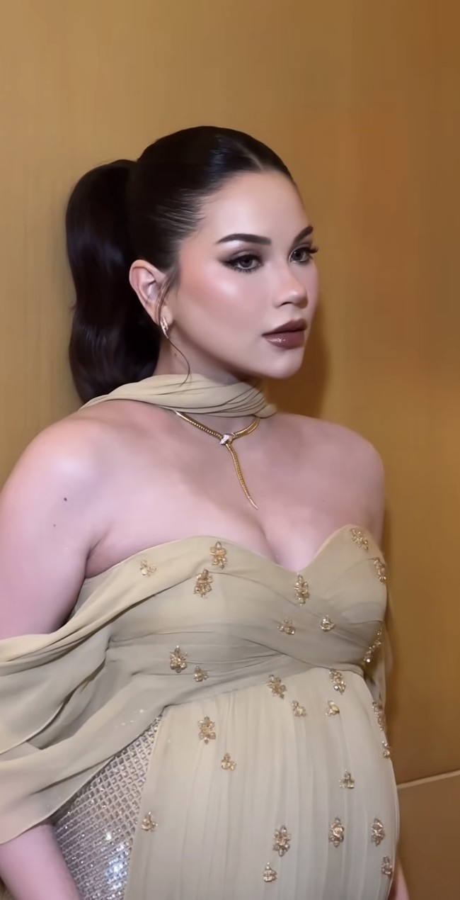Bagian atas gaun didesain strapless sweetheart neckline yang dibalut layer transparan dengan aksen drapery di bahu, menciptakan efek off-shoulder yang anggun. Gaun tersebut juga dihiasi embellishment kecil berwarna senada yang tersebar, memberikan kilau tanpa terlihat berlebihan. Foto: Instagram/@rhay_david