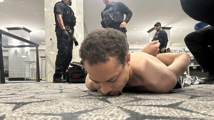 Tersangka Cole Tomas Allen terlihat terbaring di atas karpet. Kedua tangannya diborgol ke belakang, sementara sejumlah petugas kepolisian berdiri di sekelilingnya. (Donald Trump)

