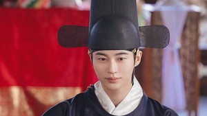 Pangeran Agung Ian di sisi lain tampil dalam busana berwarna lebih kalem, tetap dengan aksen emas di dada. Dia mengenakan topi tinggi dengan sayap di bagian kanan-kiri. (Foto: dok. MBC)