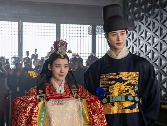 Keduanya tampak elegan memakai baju pernikahan tradisional kerajaan Korea, berhias ornamen emas. IU berbalut jubah berwarna merah lengkap dengan jokduri alias mahkota di atas kepala. Sementara Byeon Woo Seok memakai jubah biru tua dengan samo, sejenis topi berwarna hitam. Foto: dok. MBC