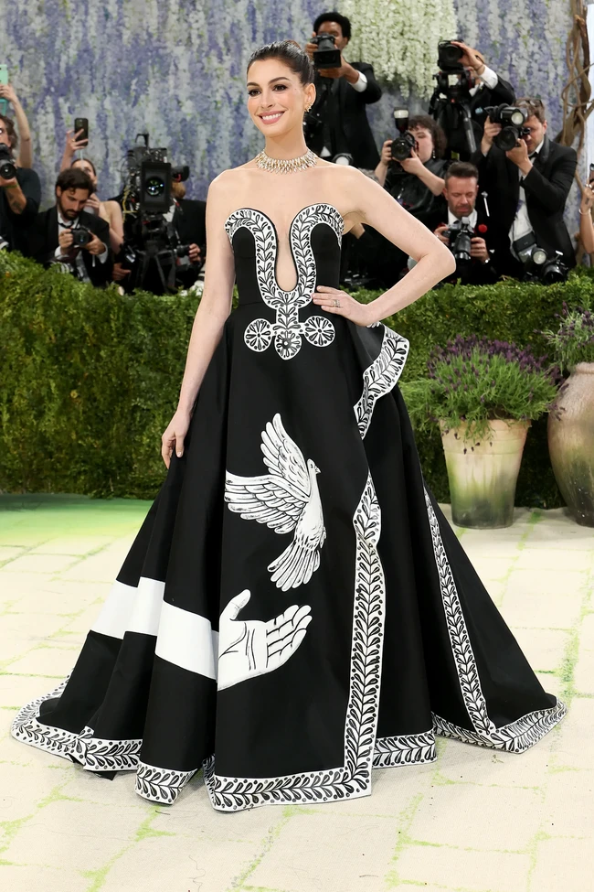 Anne Hathaway tampil elegan dalam gaun custom Michael Kors hasil kolaborasi dengan seniman Peter McGough, di mana gaun hitam strapless itu menjadi kanvas lukisan tangan penuh simbol perdamaian, flora, dan narasi puitis yang terinspirasi dari Ode on a Grecian Urn, memadukan siluet klasik dengan storytelling artistik. Foto: Getty Images