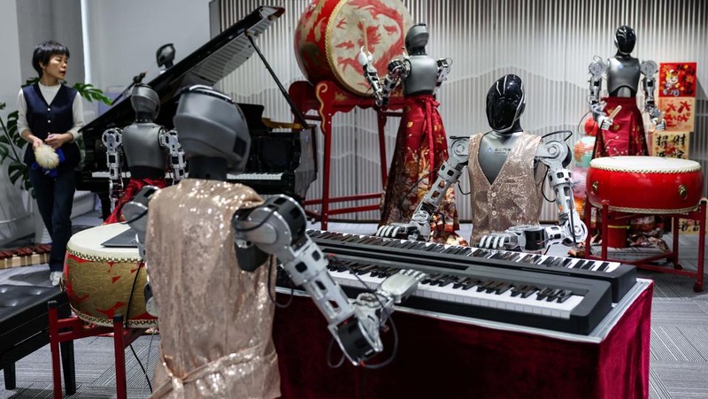 An ensemble of humanoid robots produced by Linkerbot is set up with musical instruments as a woman holding a wipe walks nearby, at the company’s office in Beijing, China, April 27, 2026. REUTERS/Maxim Shemetov