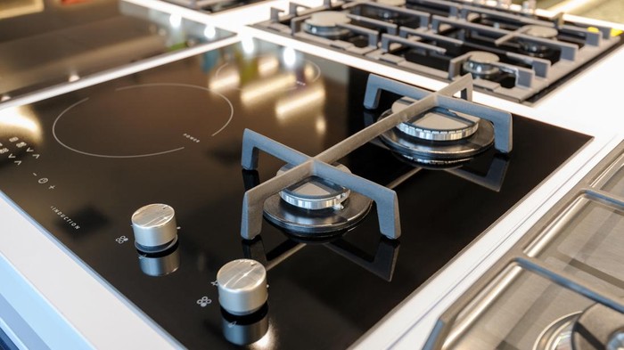 Hybrid gas and electric induction stove with black glass tray selling in appliance retail store showroom, closeup, selective focus