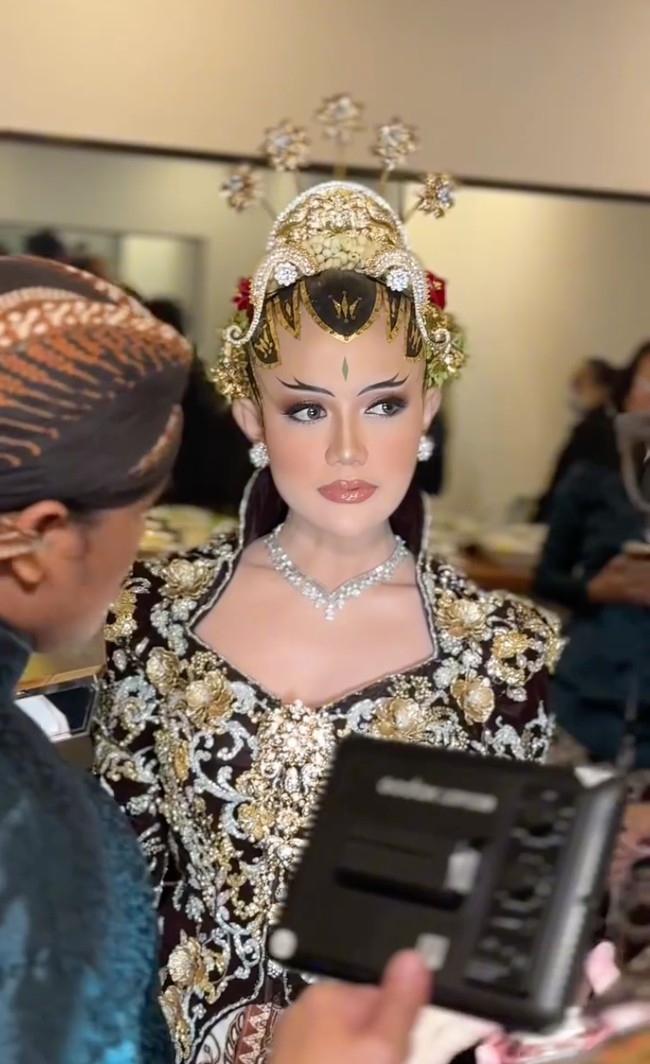 Nuansa tradisional semakin lengkap dengan paes dan sanggul di kepala menantu Soimah, Yosika Ayumi. Ia juga menambahkan beberapa perhiasan berkilau berukuran cukup besar yang membuat tampilannya semakin terlihat mewah. Foto: Instagram/@ivan_gunawan