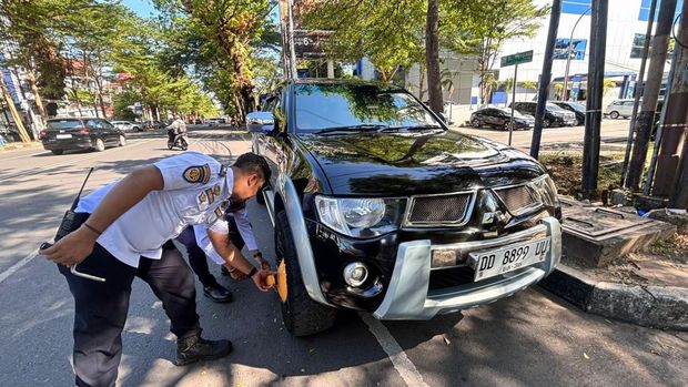 Petugas Dishub Makassar menggembok mobil yang parkir liar di badan jalan.