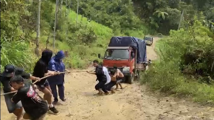 Sejumlah warga di Kabupaten Enrekang, Sulawesi Selatan (Sulsel), menarik sebuah truk melewati jalan menanjak yang rusak dan berlumpur.