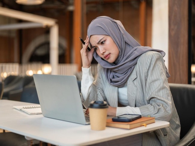 Troubled asian muslim woman student holding head looking at laptop sitting with book at cafe table. Everyday life, Modern tech, Chilling Outdoors.