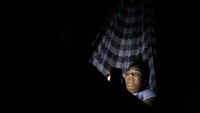 Seorang warga menggunakan telepon genggam di atas hammock saat listrik padam di Valencia. Banyak masyarakat mengandalkan cahaya ponsel dan baterai cadangan untuk beraktivitas malam hari di tengah blackout yang semakin sering terjadi. REUTERS/Juan Carlos Hernandez