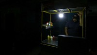 Seorang pedagang tetap melayani pembeli di kios dengan pencahayaan minim saat pemadaman listrik di Valencia. Usaha kecil menjadi salah satu sektor yang paling terdampak karena banyak pelaku usaha harus tetap beroperasi di tengah ketidakstabilan pasokan listrik. REUTERS/Juan Carlos Hernandez