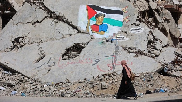A woman walks past a mural depicting football player Lamine Yamal waving a Palestinian flag during the Catalans title parade, painted by Palestinian artists on the rubble of buildings destroyed during the war, at Shati (Beach) refugee camp in Gaza C
