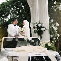 Dhani dan Nada tampil serasi saat berdiri di atas mobil Baic putih yang dihias pita besar, menciptakan momen wedding car yang modern, gagah, sekaligus tetap terlihat elegan. Foto: Dok. Instagram @thepotomoto.