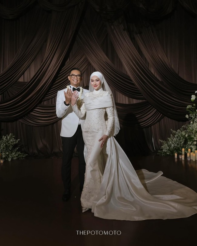 Di hari pernikahannya, Indah Nada Puspita mengenakan busana cantik siluet mermaid rancangan desainer Malaysia, Rizman Ruzaini Bridal. Pada bagian bahu dan dada, terdapat detail potongan Draped Off-Shoulder atau aksen wrap berbahan satin yang melilit rapi, memberikan kesan modern sekaligus menyamarkan sambungan hijab pada kerah baju. Foto: Dok. Instagram @thepotomoto.
