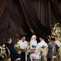 Pernikahan ini mengusung dekorasi bergaya klasik elegan dengan latar belakang tirai kain drapery berwarna cokelat tua yang megah, dipadukan dengan sentuhan romantis dari pencahayaan lilin hangat dan aransemen bunga putih yang anggun di sudut ruangan dari Artluxe Decor @artluxedecor. Foto: Dok. Instagram @thepotomoto.
